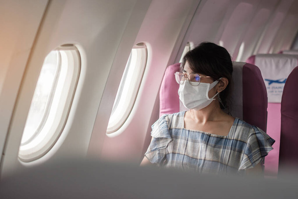 Uçakta ya da toplu taşımada koruyucu yüz maskesi takan genç bir kadın, Coronavirus hastalığı enfeksiyonunu koruma, seyahat etmeye hazır Asyalı bir turist. Sonraki Normal ve yeniden açılan konsept - Fotoğraf, Görsel