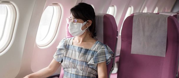 Νεαρή γυναίκα που φοράει προστατευτική μάσκα προσώπου σε αεροπλάνο ή μέσα μαζικής μεταφοράς, προστασία από τη μόλυνση από τον ιό του Coronavirus, Ασιάτης τουρίστας έτοιμος να ταξιδέψει. Επόμενο Normal και επαναλειτουργία - Φωτογραφία, εικόνα