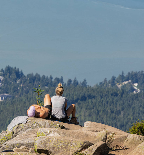 Nuori pariskunta istuu kalliolla ja nauttii näkymistä Eagle Bluffsista Cypressin maakuntapuistossa Kanadassa. Concept valokuva vaellus, kopioi tilaa teksti, valikoiva keskittyä, matka valokuva. - Valokuva, kuva