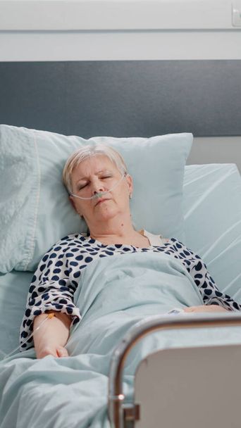 Літня жінка з IV крапельницею спить у лікарняному ліжку
 - Фото, зображення