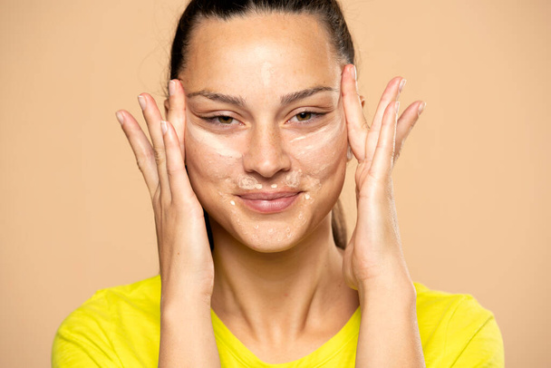 Primo piano della giovane donna applica correttore sul suo viso su uno sfondo beige - Foto, immagini