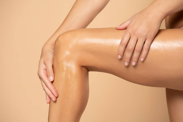 Primo piano su una donna che applica la crema sulle gambe su sfondo beige - Foto, immagini