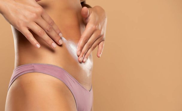woman applying stretch marks cream on her belly on a beige background - Photo, Image