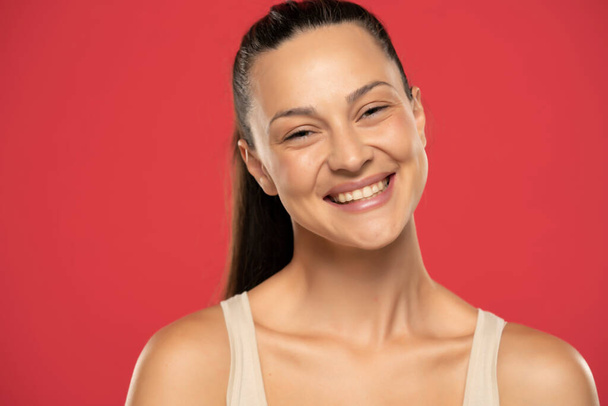 Muotokuva kaunis hymyilevä nainen sidottu hiukset punaisella pohjalla - Valokuva, kuva