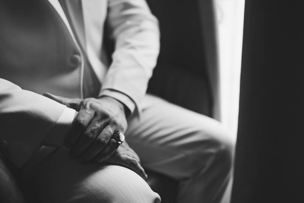Egy öltönyös férfi, pecsétgyűrűvel a kisujján ül az ablak mellett, közelről, fekete-fehér. - Fotó, kép