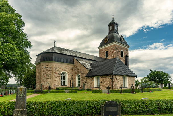 Hermosa iglesia antigua ubicada en San Skedvi en Suecia, y un cementerio muy bien cuidado con filas de lápidas y flores de colores. En un hermoso día de verano con frondosos árboles verdes, la luz del sol y un cielo azul - Foto, imagen