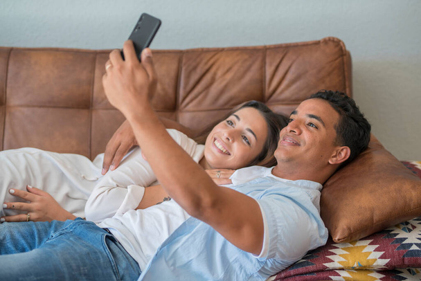 Happy romantic adult young interracial couple enjoy life at home taking selfie pictures for social media. - Photo, image