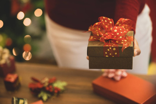 Persoon op trui dragen prachtige geschenkdoos met mooie strik en aantrekkelijke foto 's per smartphone te onthouden gelukkige moment van cadeau geven, liefde delen, en zoete viering in de winter.party - Foto, afbeelding