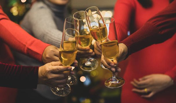 Women on sweater clink glass of beverage together to start holiday event of jolly drink at gala party for celebrating group success, cheerful relationship Add some noise to fit vintage-style image. - Photo, Image