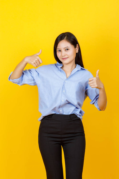 Cute and young Japanese style girl standing and raise hand show thumbs up with smile face on yellow background. - Foto, Imagem