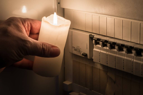Sulakerasia sulakkeineen jakelulaatikossa sähkökatkoksen aikana valaistu valkoinen kynttilä hallussa mies, Saksa - Valokuva, kuva