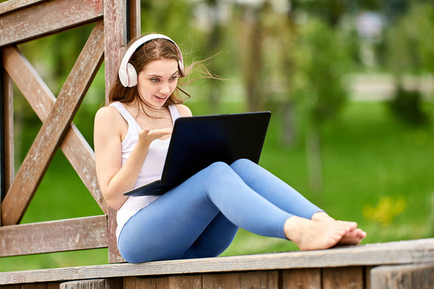 Kobieta używa laptopa do wideokonferencji z przyjaciółmi w parku publicznym. - Zdjęcie, obraz