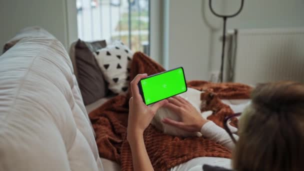 Женщина лежит на диване и смотрит онлайн видео на смартфоне с хрома-ключом - Кадры, видео