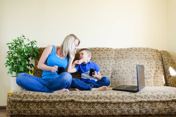 Mother and small child, boy at home sitting on couch, using laptop, relax. Working from home. Happy family lifestyle, hobby and leisure. Business woman concept - Photo, image