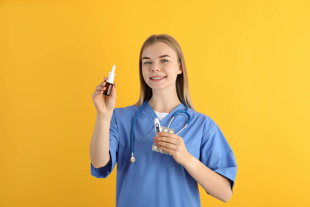 Young nurse with nasal spray on yellow background, seasonal cold treatment - Photo, Image