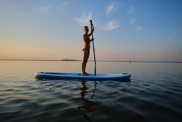 Siluet of Woman standing on SUP board and paddling through shining water surface. Wide shot Version 8 - Foto, immagini