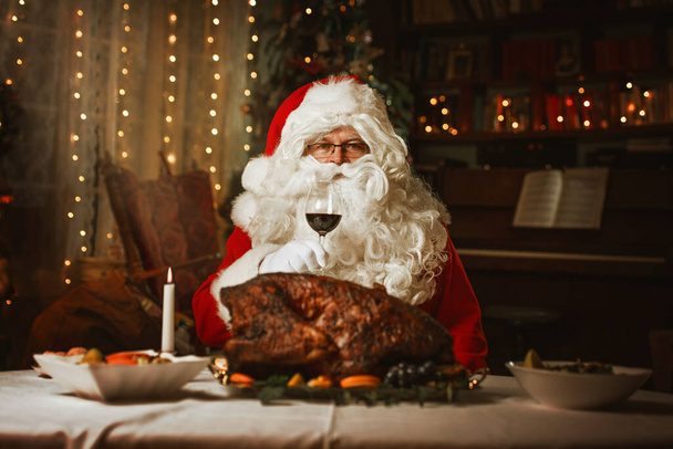 Santa Claus sitting at a table, eating a turkey - Fotoğraf, Görsel
