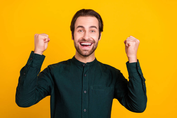 Photo of funny lucky young man wear smart casual outfit smiling rising fists isolated yellow color background - Фото, изображение
