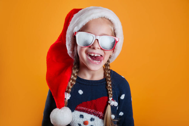 Funny little girl in Santa Claus hat and sunglasses having fun. Happy New Year and Merry Christmas - Foto, Imagem
