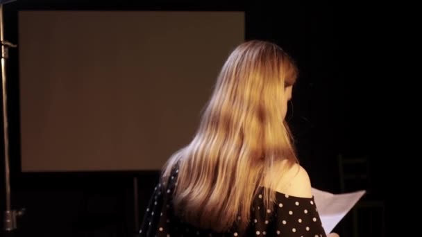 Молодая актриса на кастинге пересматривает текст и практикует свою роль стоя в темной комнате - Кадры, видео