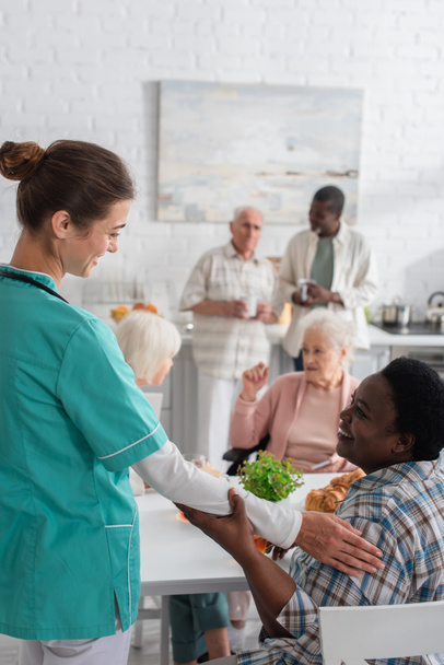 Lächelnde Krankenschwester berührt ältere Afroamerikanerin in Pflegeheim  - Foto, Bild