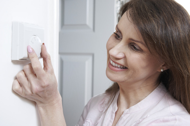 Woman Adjusting Thermostat On Central Heating Control - 写真・画像