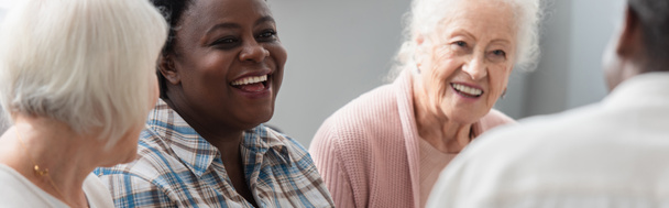 老人ホームで高齢者の友人と話すアフリカ系アメリカ人女性の笑顔,バナー  - 写真・画像