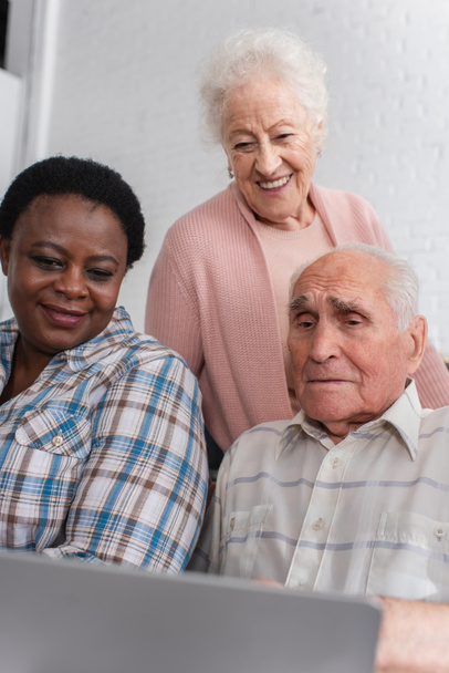 Elderly multiethnic pensioners looking at blurred laptop in nursing home  - Foto, afbeelding