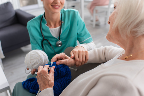 Femme âgée tricot près floue infirmière souriante en uniforme dans la maison de soins infirmiers  - Photo, image