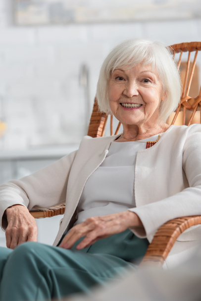 Fröhliche Seniorin blickt im Schaukelstuhl im Pflegeheim in die Kamera  - Foto, Bild