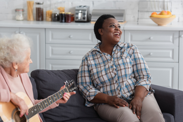 African american woman singing near senior friend playing acoustic guitar in nursing home  - Foto, Bild