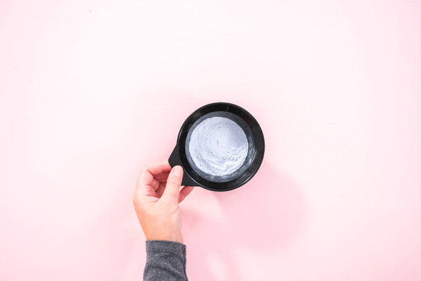 Flat lay. Hair color dye powder in a black plastic mixing bowl on a pink background. - Valokuva, kuva