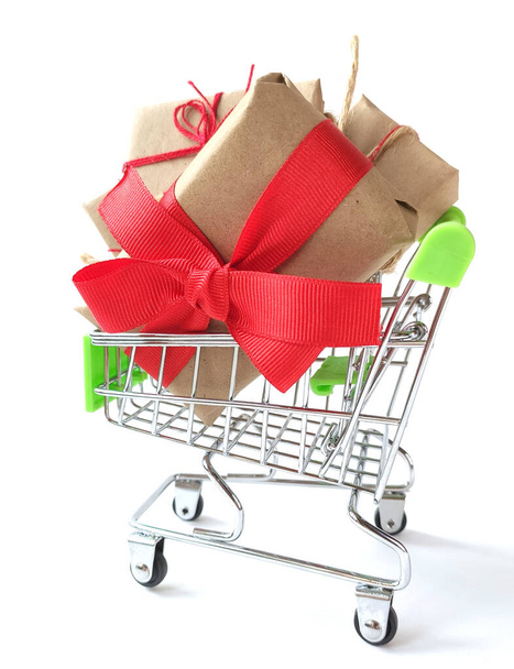 Shopping trolley with gifts isolated on a white background. Gifts wrapped in kraft paper with red ribbons and bow. Creative concept for sale. - Fotoğraf, Görsel