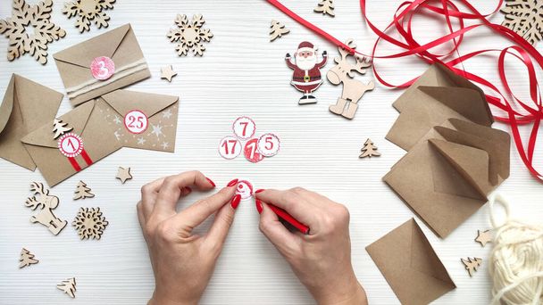 Woman makes Christmas advent calendar for kids. Writes a number for the calendar with red pencil. Step by step instruction. Step 4. Top view. - Photo, image