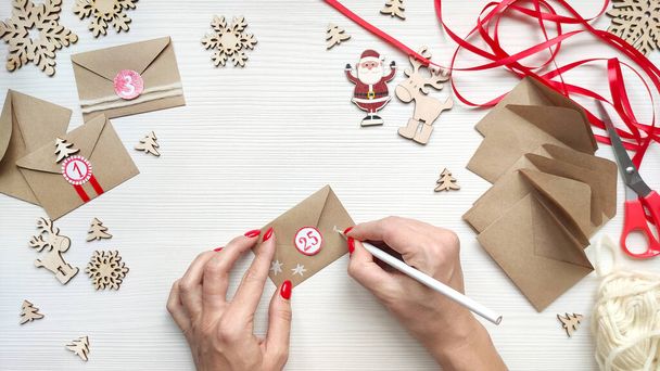 Woman makes Christmas advent calendar for kids. Decorates the envelope, draws stars with a white pencil. Step by step instruction. Step 5. Top view. - Photo, image