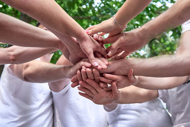 A diverse group of people on corporate teambuilding party. Stacking hands, partners standing outdoors. - Foto, imagen