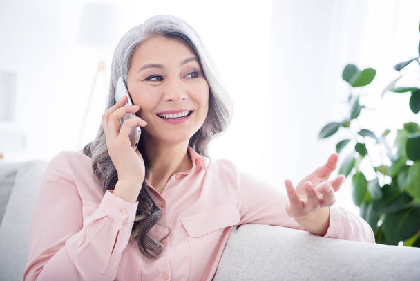 Photo of dreamy happy old woman talk phone good mood smile sit sofa indoors inside house home apartment - Фото, изображение