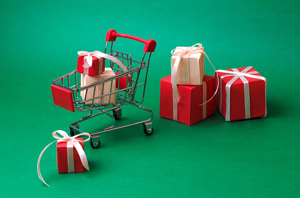 Su uno sfondo verde scuro, un carrello del supermercato pieno di regali festivi. Preparazione per le vacanze invernali, vacanze. Capodanno sconto.Shopping online - Foto, immagini