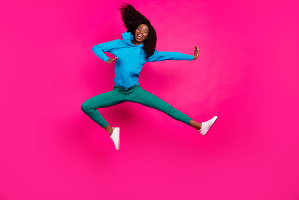 Photo of charming funky dark skin lady wear blue hoodie jumping high like ninja smiling isolated pink color background - Фото, изображение