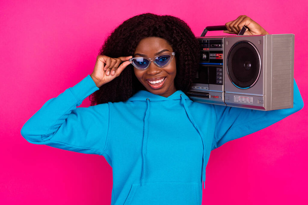 Photo of cool sweet dark skin woman dressed blue sweatshirt arm eyewear smiling listening boombox isolated pink color background - 写真・画像