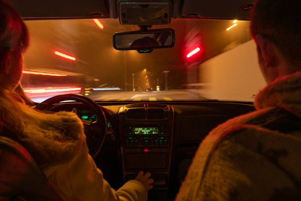Auto jezdí v noci. Uvnitř výhledu na auto, kavkazská žena řidič a muž pasažér, oba nerozeznatelný. Rozmazané venkovní světlo, pohyblivý výstřel, dlouhé vystavení. Osvětlená přístrojová deska. - Fotografie, Obrázek