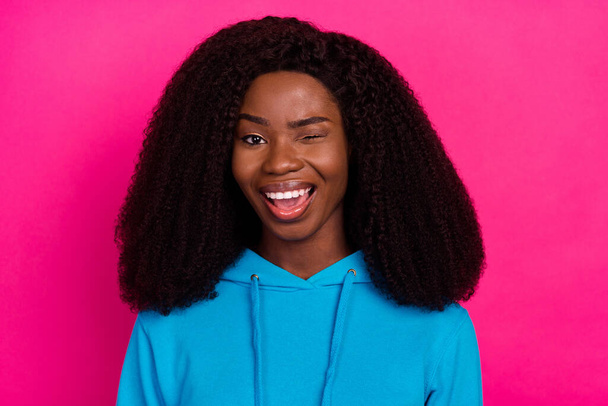 Photo of impressed flirty dark skin lady wear blue hoodie open mouth winking smiling isolated pink color background - Fotó, kép