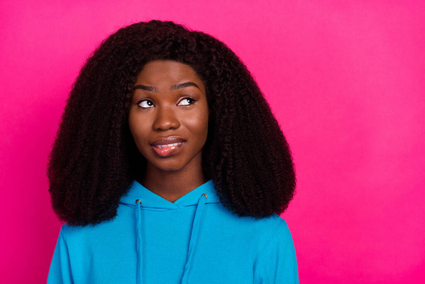 Photo of funny doubtful dark skin woman dressed blue sweatshirt biting lip looking empty space isolated pink color background - Foto, Imagem