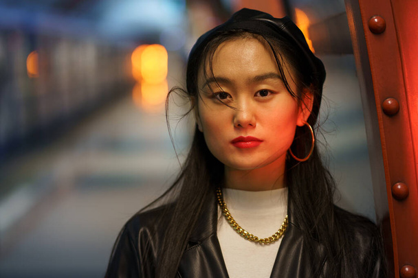 Городской портрет китайской женщины носит кожаный берет и куртку, серьги на платформе метро - Фото, изображение