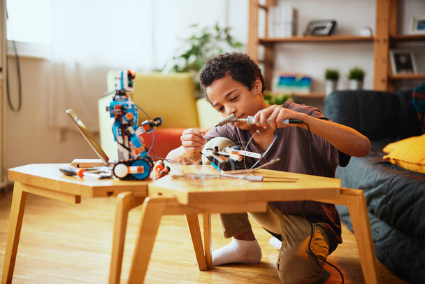 Een Afro-Amerikaanse jongen die thuis een robot maakt. Onderwijs in robottechniek thuis. - Foto, afbeelding