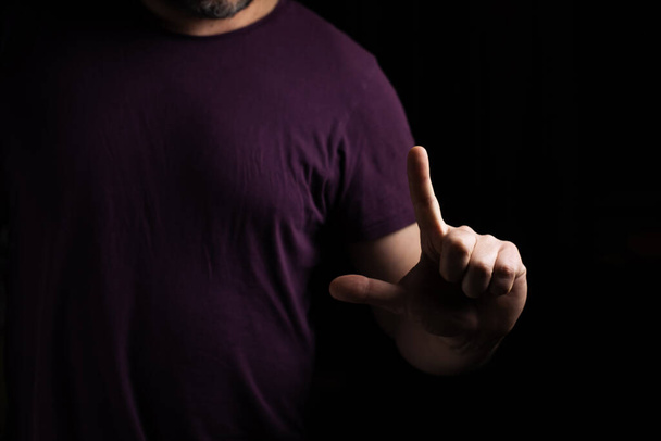 A man in a T-shirt holds an index finger up against a dark background. - Photo, image