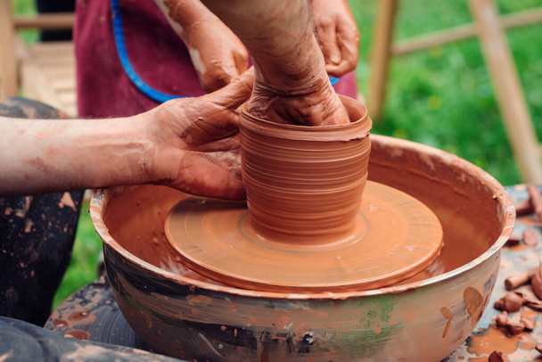 Potter enseigner à l'enfant à faire pot en céramique sur la roue de la poterie. Atelier de poterie dehors. Des potiers et des mains d'enfants. Famille travaillant sur la roue de poterie. Papa et enfant faisant pot en céramique ensemble. - Photo, image