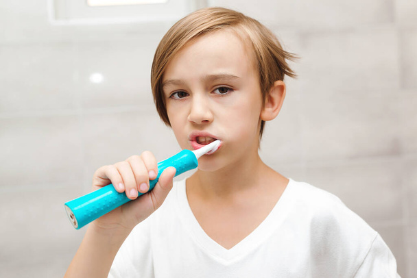 Lapsi harjaa hampaitaan sähköharjalla kylpyhuoneessa. Hammashygienia joka päivä. Terveydenhuolto, lapsuus ja hammashygienia. Poika välittää hampaidensa terveydestä. Onnellinen poika hampaiden puhdistus. - Valokuva, kuva