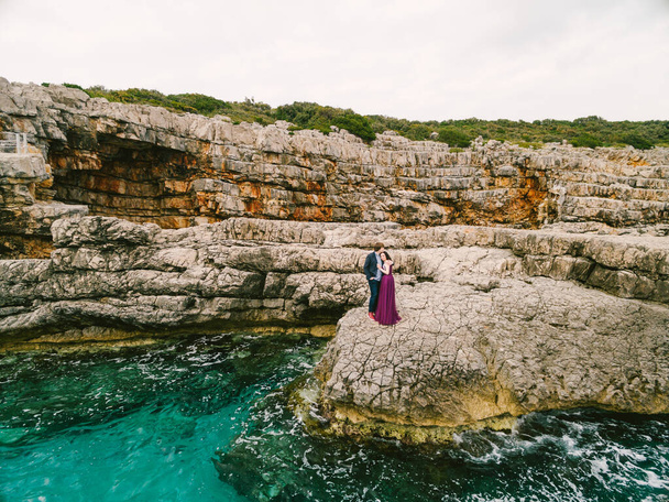 Mann und Frau umarmen sich auf den Felsen vor dem Hintergrund des brodelnden blauen Meeres. Luftaufnahme - Foto, Bild