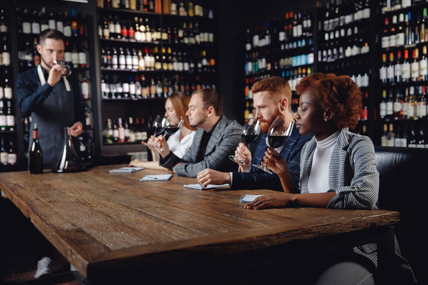 Rotweinprobe im Restaurant mit Sommelier. Gruppe von Europäern und afrikanischen Freunden verkostet Alkohol - Foto, Bild